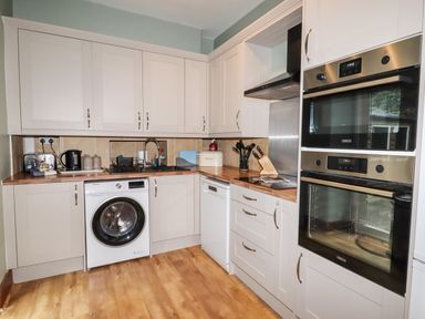 A kitchen with white cabinets wooden countertops a washing machine a dishwasher built in ovens and kitchen appliances at Ty Capel in Betws Y Coed