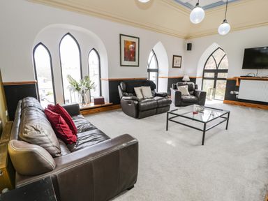 A living room with leather sofas a glass coffee table and arched windows at Greystones Chapel in Cwm-y-Glo near Llanrug