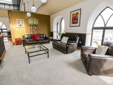 A living room with leather sofas glass coffee table and large arched windows at Greystones Chapel in Cwm-y-Glo near Llanrug