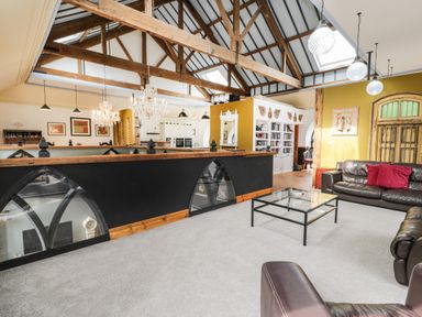 A living area with leather sofas and a glass coffee table under wooden ceiling beams at Greystones Chapel in Cwm-y-Glo near Llanrug