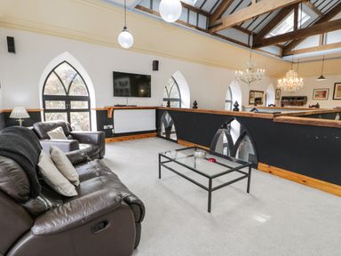 A seating area with leather sofas a glass coffee table a wall mounted tv and arched windows at Greystones Chapel in Cwm-y-Glo near Llanrug