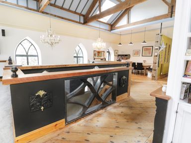 An interior space with wooden floors chandeliers arched windows a dining table and chairs at Greystones Chapel in Cwm-y-Glo near Llanrug
