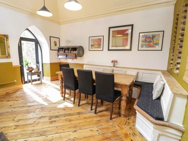A dining room with a wooden table black chairs framed artwork and a corner bench at Greystones Chapel in Cwm-y-Glo near Llanrug