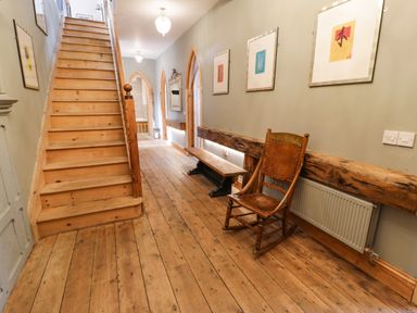 A hallway with wooden stairs a rocking chair a bench framed pictures and a mirror at Greystones Chapel in Cwm-y-Glo near Llanrug