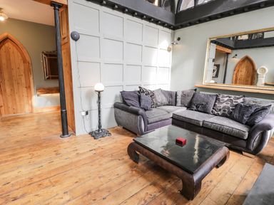 A living room with a gray sectional sofa a black coffee table and wooden floors at Greystones Chapel in Cwm-y-Glo near Llanrug
