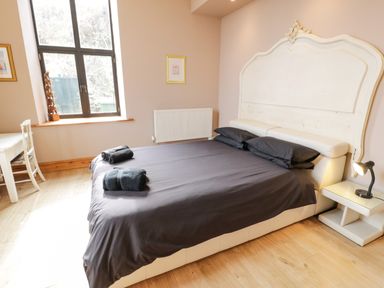 A bedroom with a large bed with black bedding and towels on it a window and a white chair beside a desk at Greystones Chapel in Cwm-y-Glo near Llanrug