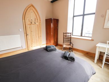 A bedroom with a wooden wardrobe a chair a window and a bed with folded towels at Greystones Chapel in Cwm-y-Glo near Llanrug