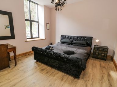 A bedroom with a black bed and pillows a wooden desk with a chair a window and a small nightstand with a lamp at Greystones Chapel in Cwm-y-Glo near Llanrug