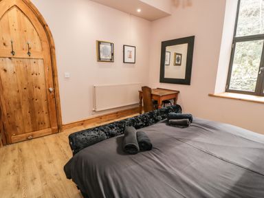 A bedroom with a wooden desk and chair a large mirror two framed pictures a wooden door and a window at Greystones Chapel in Cwm-y-Glo near Llanrug