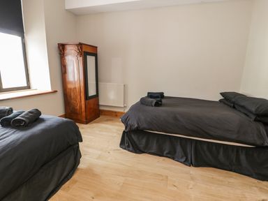 A bedroom with two beds covered in black bedding an antique wooden wardrobe and a window at Greystones Chapel in Cwm-y-Glo near Llanrug