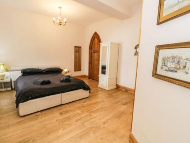 A bedroom with a double bed black bedding and rolled towels wooden floor white wardrobe and wooden door at Greystones Chapel in Cwm-y-Glo near Llanrug
