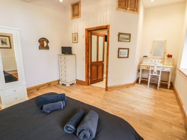 A bedroom with a bed and rolled towels a white wardrobe a small chest of drawers with a tv and a dressing table with chair at Greystones Chapel in Cwm-y-Glo near Llanrug