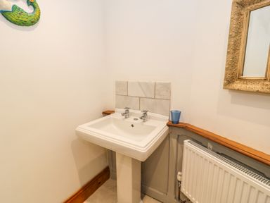A bathroom corner with a pedestal sink with two taps a blue cup a radiator and a framed mirror at Greystones Chapel in Cwm-y-Glo near Llanrug