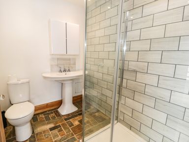 A bathroom with a toilet a pedestal sink a wall cabinet and a glass shower enclosure with tiled walls at Greystones Chapel in Cwm-y-Glo near Llanrug