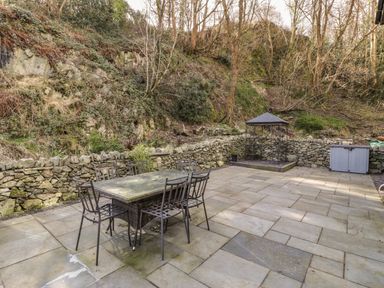 An outdoor patio with a metal table and six chairs stone walls a metal gazebo and a storage box at Greystones Chapel in Cwm-y-Glo near Llanrug