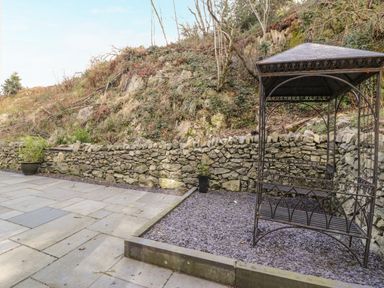 A stone paved patio with a metal gazebo a stone wall and plants at Greystones Chapel in Cwm-y-Glo near Llanrug