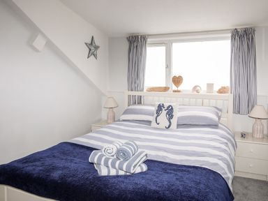 A bedroom with a bed with striped bedding and towels on it with lamps on bedside tables at Enfys in Criccieth