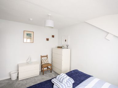 A bedroom with a bed folded towels a white chest of drawers a wooden chair and a framed picture on the wall at Enfys in Criccieth