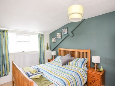 A bedroom with a wooden bed frame striped bedding and matching curtains at Enfys in Criccieth