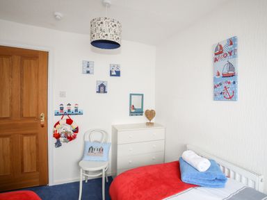 A bedroom with a wooden door a white chair with a blue cushion a white chest of drawers and a bed with blue and red towels at Enfys in Criccieth