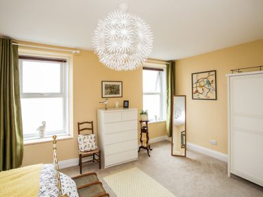 A bedroom with two windows a white dresser a chair and a wardrobe at Enfys in Criccieth