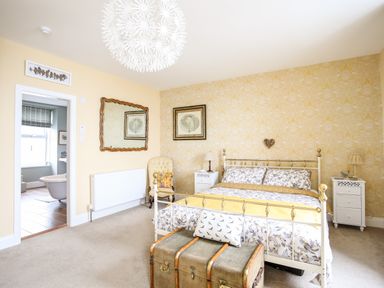 A bedroom with a metal bed frame bedside tables an armchair a large mirror and a vintage trunk at Enfys in Criccieth