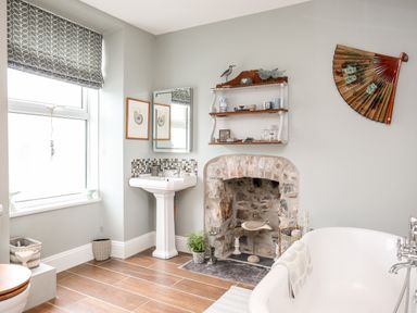 A bathroom with a bathtub sink a stone fireplace and window at Enfys in Criccieth