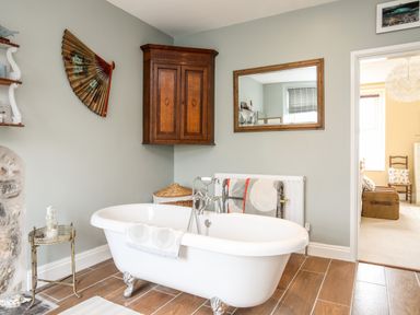 A bathroom with a freestanding bathtub a wooden cabinet a wall mirror and a side table at Enfys in Criccieth