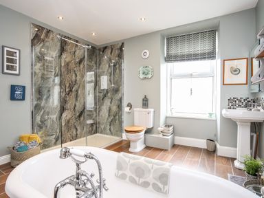 A bathroom with a bathtub shower toilet sink and a window at Enfys in Criccieth