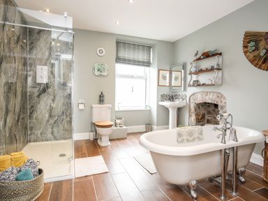 A bathroom with a freestanding bathtub shower area toilet sink and decorative shelves at Enfys in Criccieth
