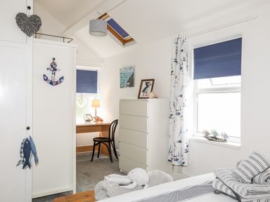 A bedroom with a white wardrobe a small desk and chair a chest of drawers and two windows at Enfys in Criccieth