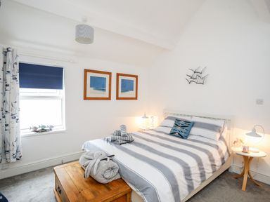 A bedroom with a double bed striped bedding wooden chest bedside tables and framed pictures on the wall at Enfys in Criccieth