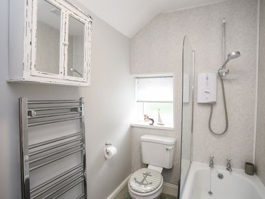 A bathroom with a toilet a bathtub with shower a towel rack and a wall cabinet at Enfys in Criccieth