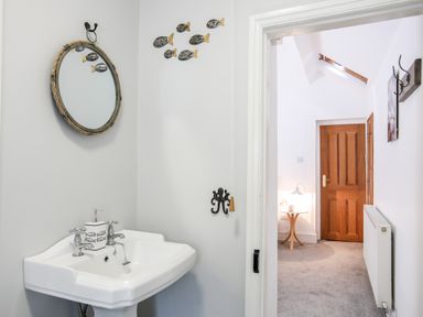 A bathroom sink with a mirror and fish wall decorations next to a hallway with wooden doors and a small table with a lamp at Enfys in Criccieth