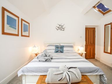 A bedroom with a bed with striped bedding two framed pictures on the wall bedside tables with lamps a wooden door a mirror and a skylight at Enfys in Criccieth