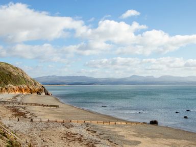 A coastal beach with a rocky cliff and wooden groynes along the shore at Enfys in Criccieth