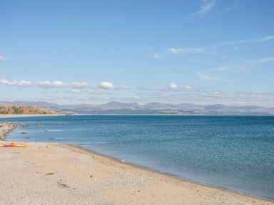 A sandy and pebbly beach with kayaks on the shore and distant hills across the water at Enfys in Criccieth