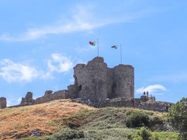A stone castle ruin on a hill with two Welsh flags flying at Enfys in Criccieth