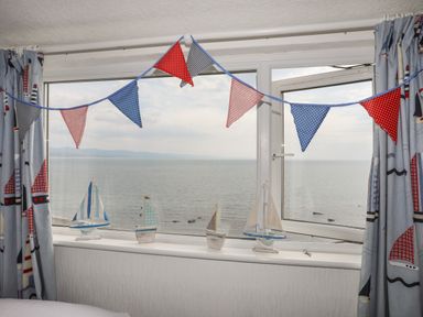 A window with model sailboats on the sill and red blue and white bunting hanging with a sea view at Enfys in Criccieth