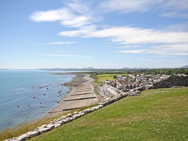 A coastal town with houses near a rocky beach and a grassy area with stone walls at Enfys in Criccieth