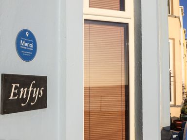 A cottage wall with Enfys nameplate and Mengi Holiday Cottages blue plaque in Criccieth