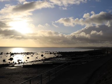 A rocky beach with a railing-lined walkway under a cloudy sky at Enfys in Criccieth