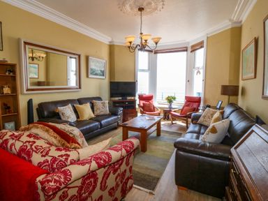 A living room with sofas a wooden coffee table two red armchairs a tv and a large window at Enfys in Criccieth