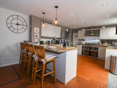 A kitchen with a wooden breakfast bar and four wooden chairs with cushions at Enfys in Criccieth