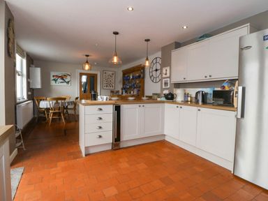 A kitchen with white cabinets wooden countertops pendant lights and a dining table with chairs at Enfys in Criccieth