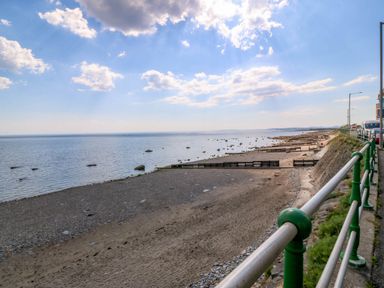 A beachfront with a sandy and pebbly shore next to a rail and road at Enfys in Criccieth