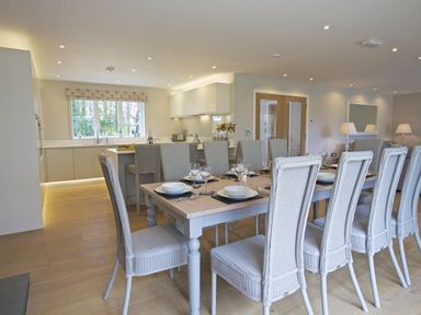 A dining area with a long table set with plates and glasses and a kitchen with bar stools at 3 The Drive Hillfield Village in Dartmouth