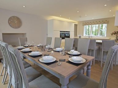 A dining area with a large wooden table set with plates and glasses surrounded by chairs and bar stools at 3 The Drive Hillfield Village in Dartmouth