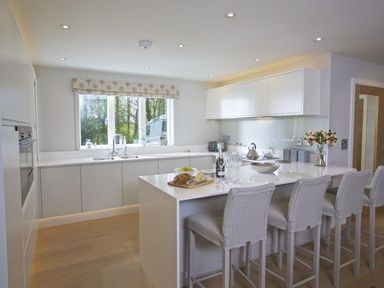 A kitchen with a countertop island and four chairs with fruit bread and wine at 3 The Drive Hillfield Village in Dartmouth