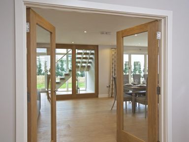 A room with wooden double glass doors leading to a space with a modern wooden staircase and a dining area with a set table at 3 The Drive Hillfield Village Dartmouth
